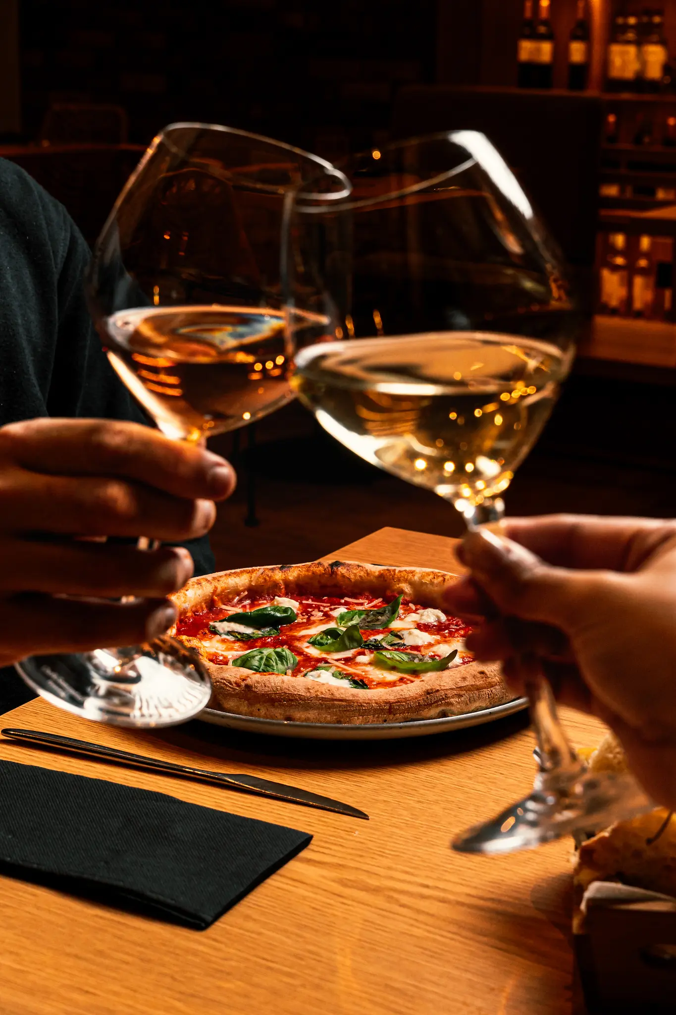 Casal a jantar pizza no restaurante e a brindar com copo de vinho branco.